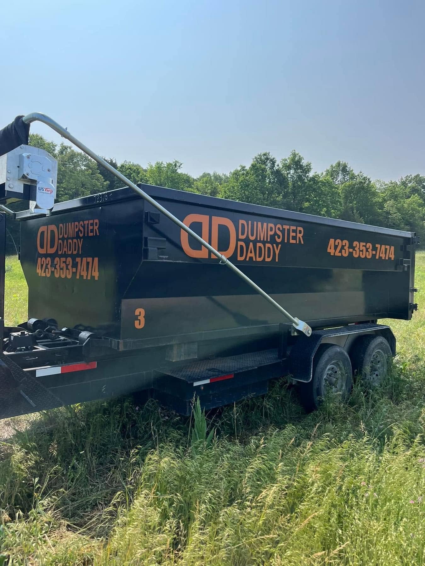 Dumpster Daddy dumpster numbered 3 on a trailer in a grassy field