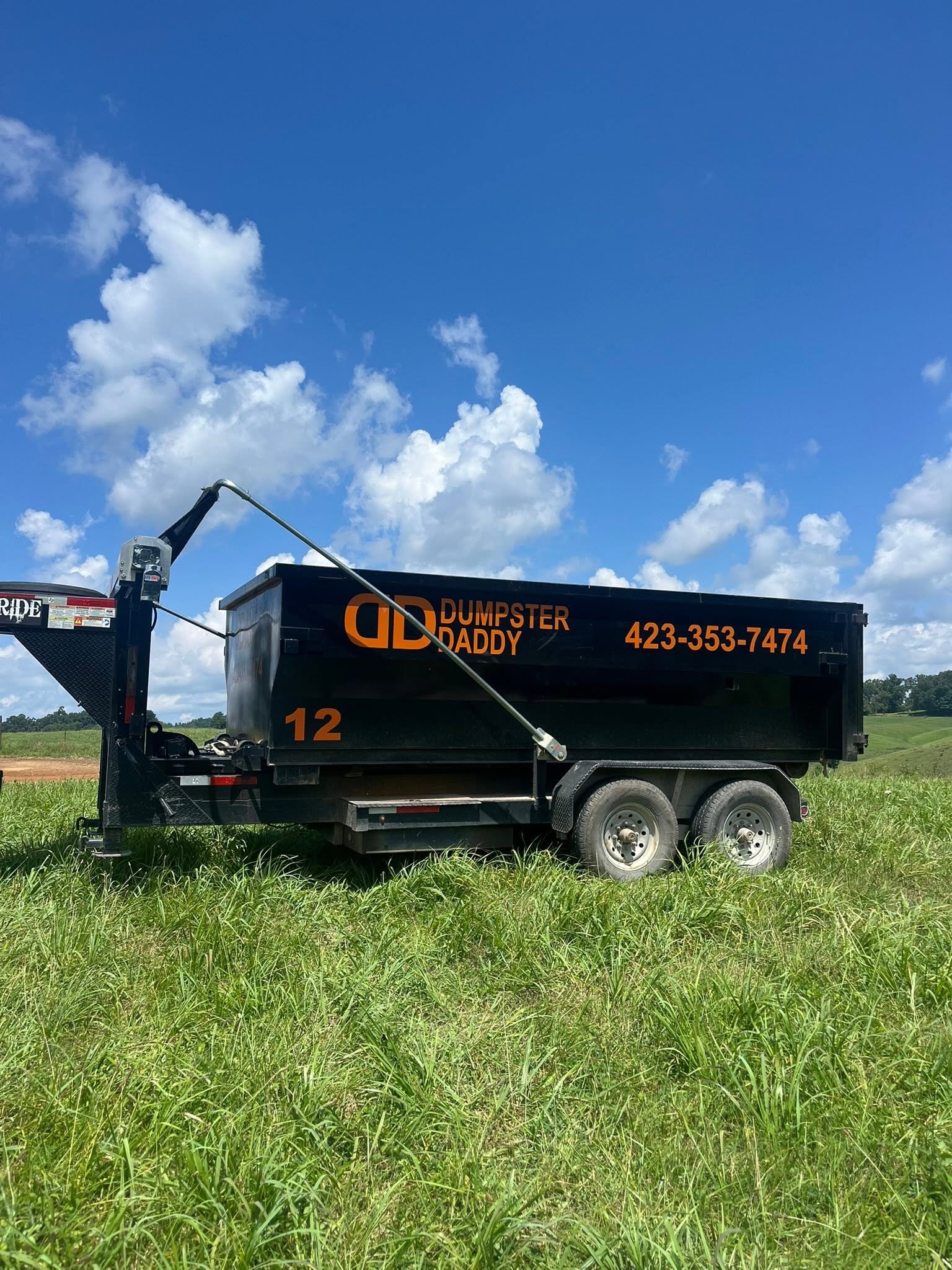 Dumpster Daddy dumpster numbered 12 parked in a green field under a blue sky